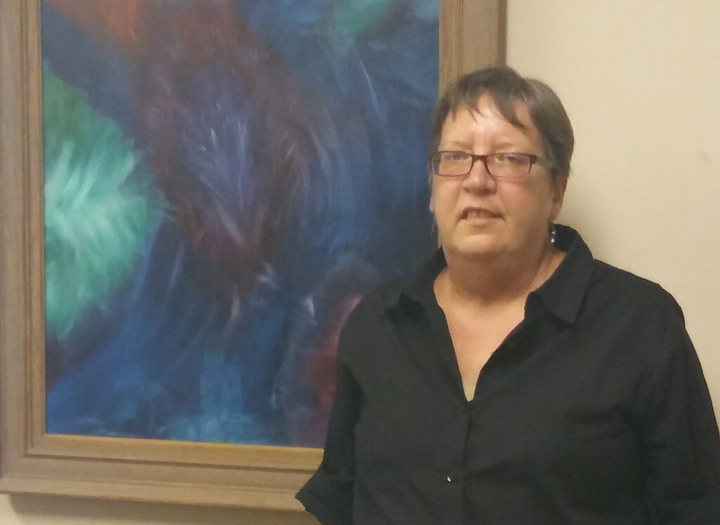 Sue Degraw: A Long Road Home 6 a woman standing in front of a painting