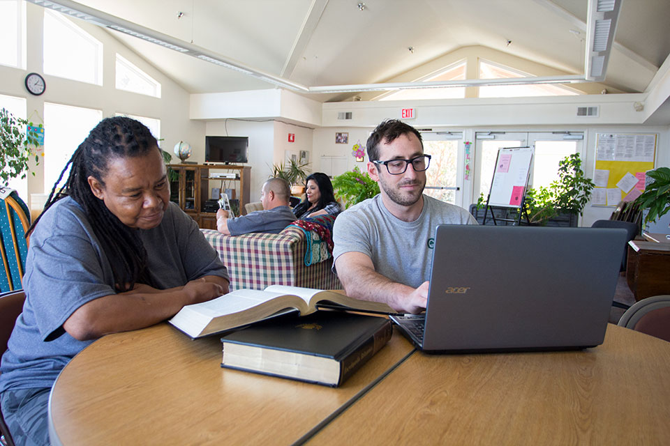 a man and woman sitting at a table with a laptop and books